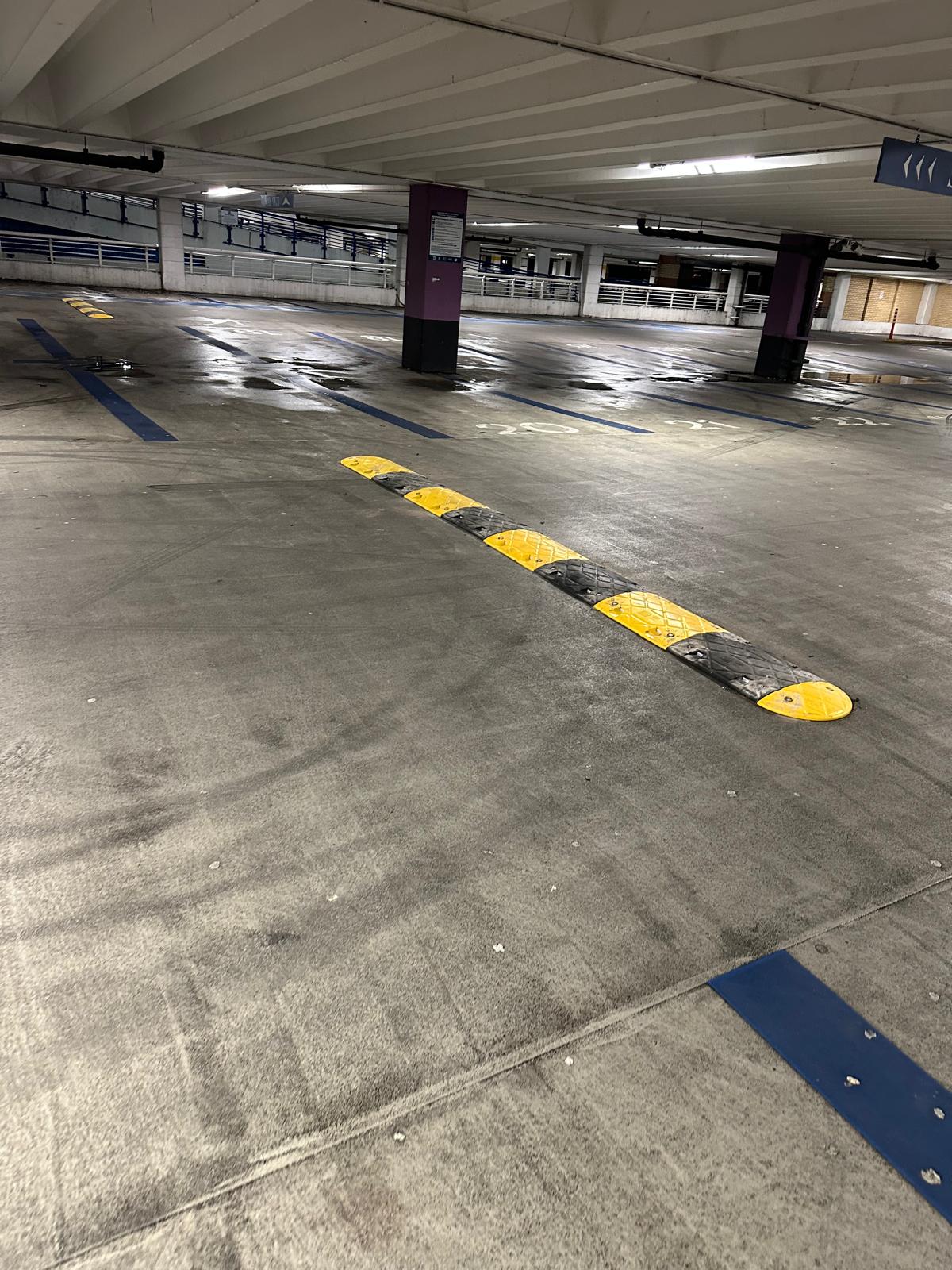 Yellow and black rubber speed bump installed on a wet concrete multi-storey car park deck