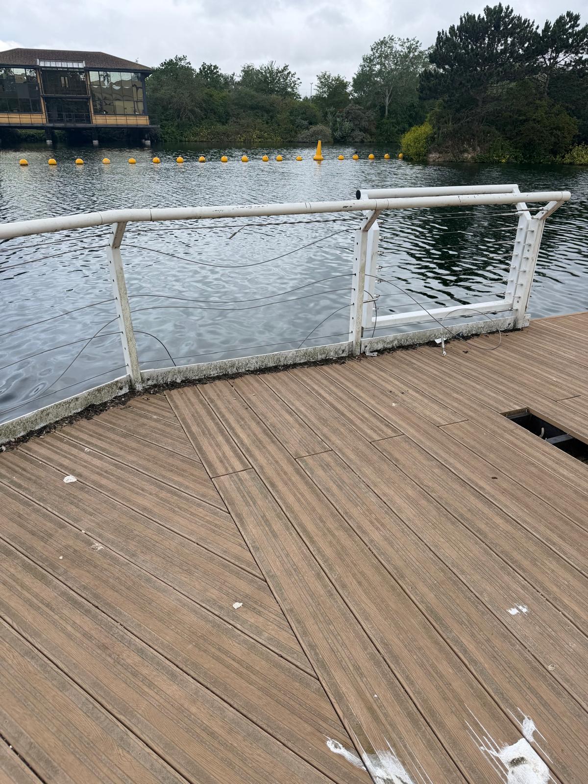 Lake side timber deck with sagging and missing safety wires in a white metal balustrade