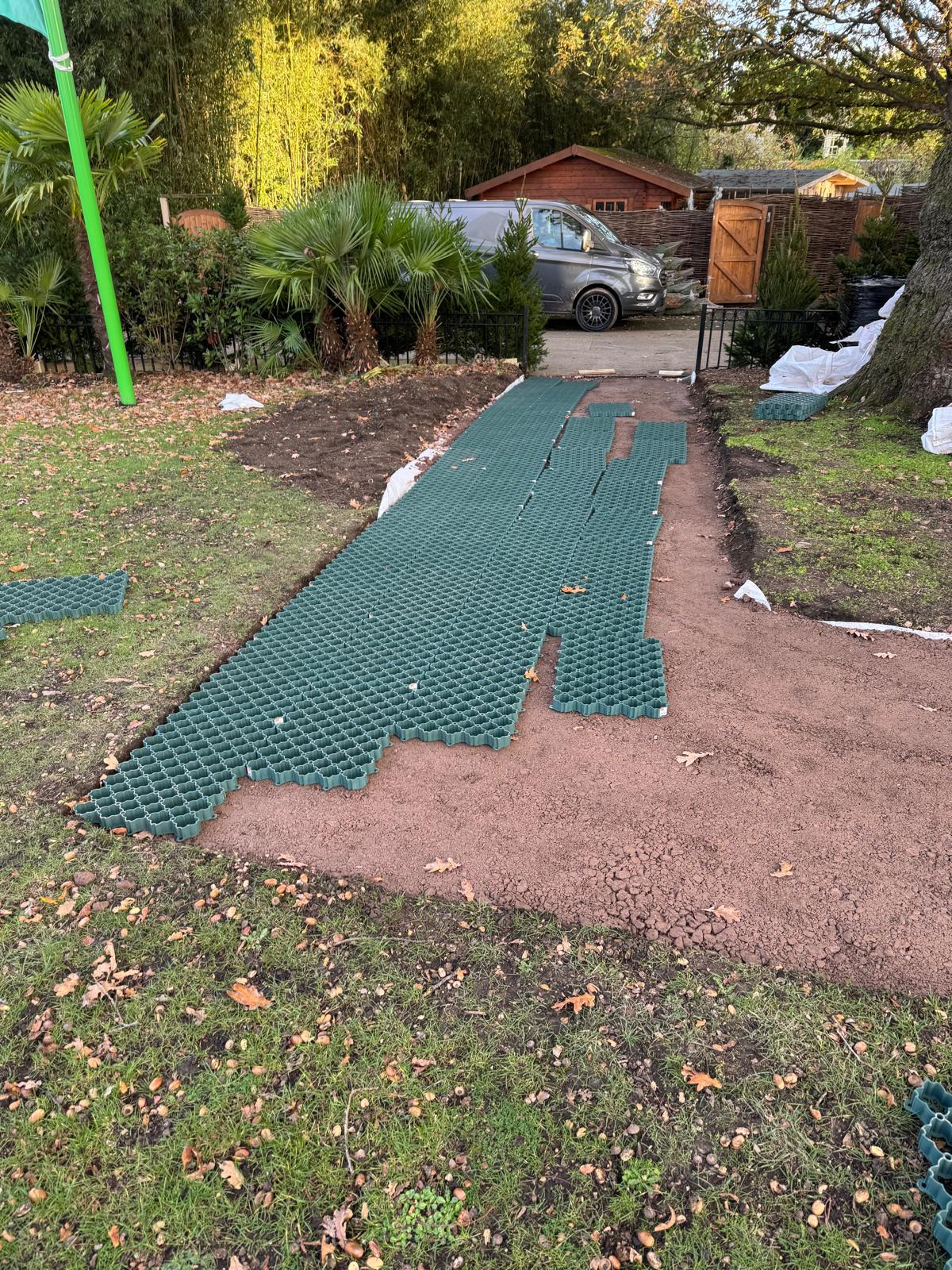 Green plastic grass reinforcement grids being laid on a compacted sand footpath base