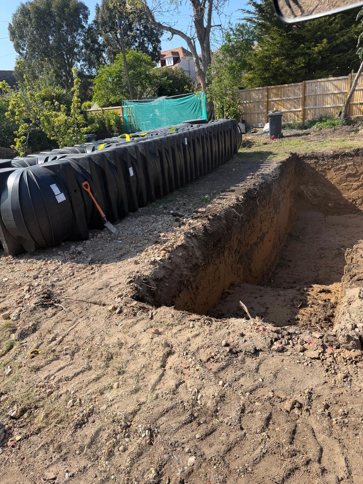 Deep excavated trench prepared beside a modular black rainwater harvesting tank