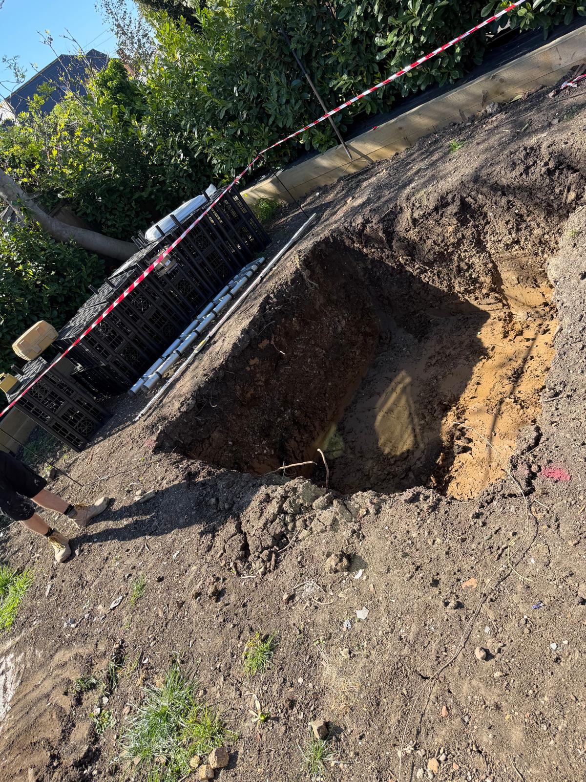 Square soakaway pit excavated in a garden with plastic drainage crates stacked nearby